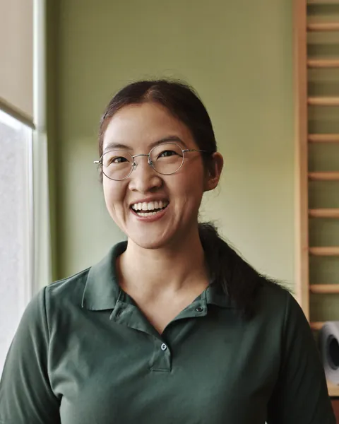 Portrait of Grace Huang, laughing, with glasses and a low ponytail, in a green clinic polo.