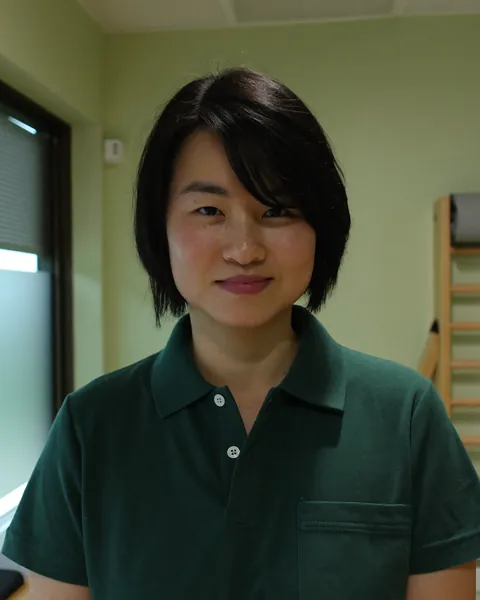 Portrait of Mei Lin, a woman with a short black bob in a green clinic polo, in a treatment room.