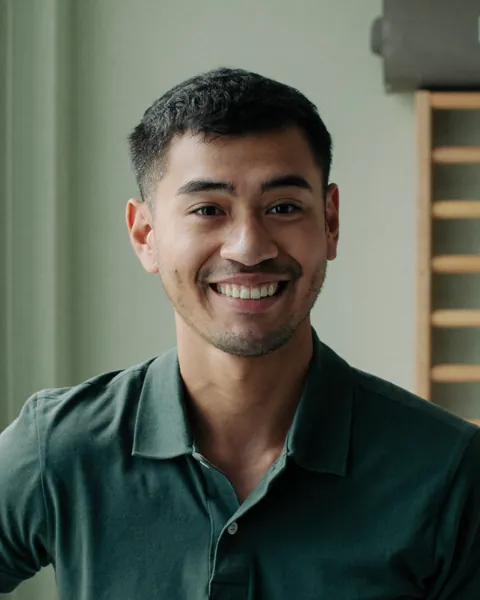 Portrait of Tom Reyes, smiling, in a green clinic polo, with wall bars behind him.